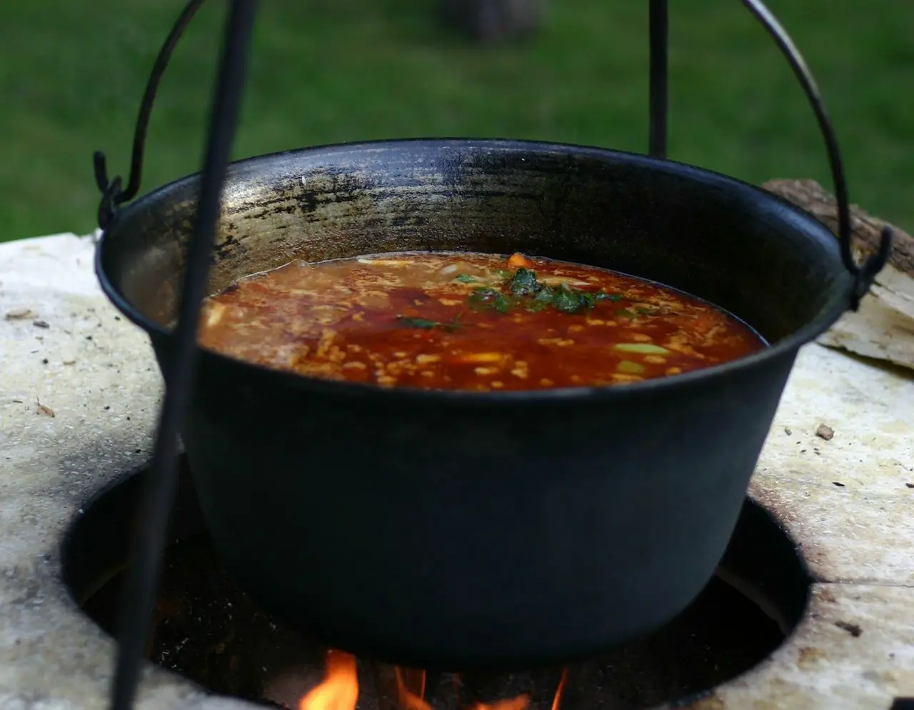 Soup is being cooked in a large hanging pot.